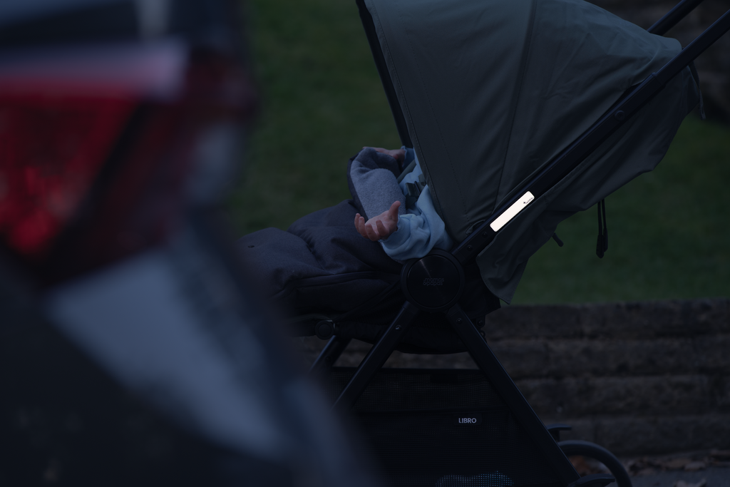 Reflective pram sticker visible on pram frame at night with car headlights in background