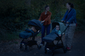 Two parents walking prams with Twinkle Safe reflective pram stickers glowing at dusk in a park