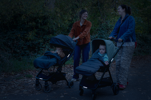 Two parents walking prams with Twinkle Safe reflective pram stickers glowing at dusk in a park